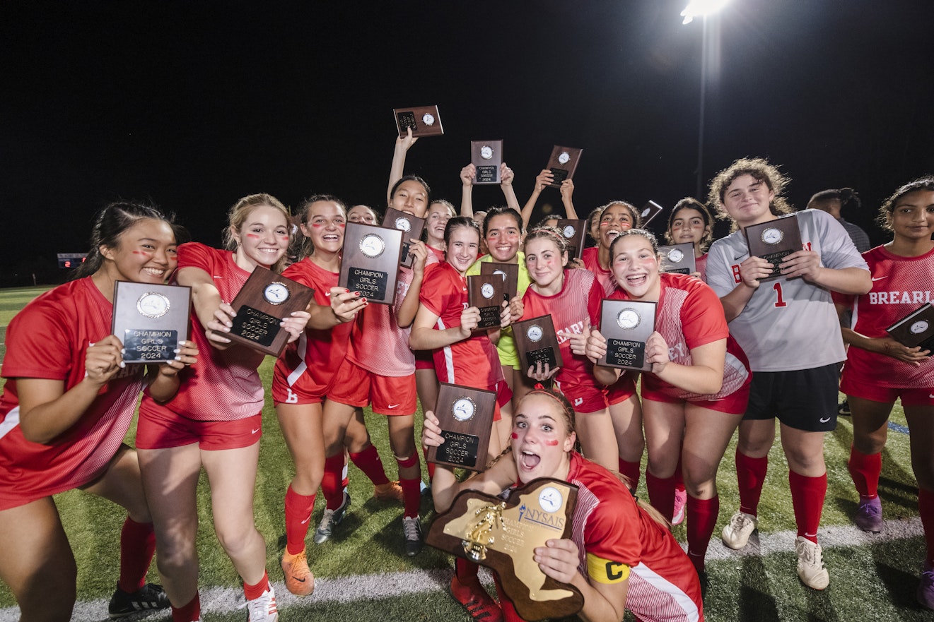 Varsity Soccer team members posing with their trophies and plaques after winning their league championship.