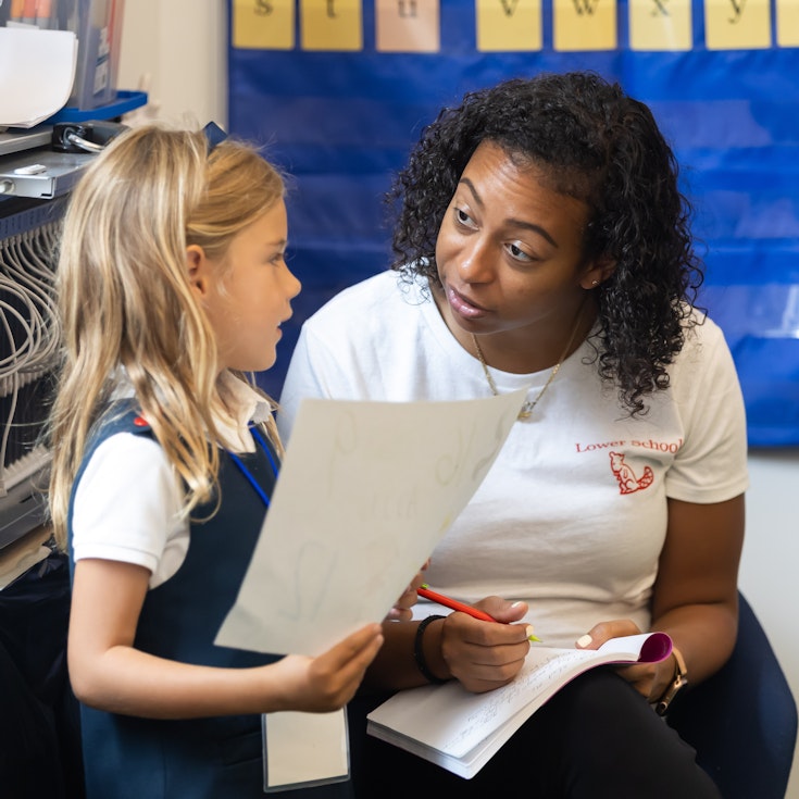 A lower school teacher speaking encouragingly to a student who is holding her classwork in her hands.