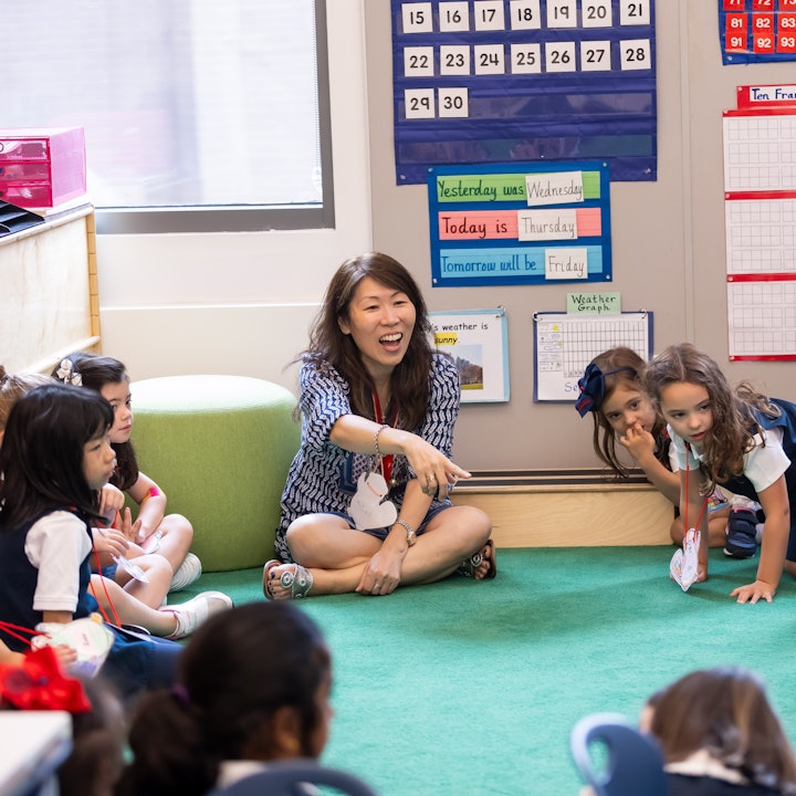 Kindergarten teacher on the floor in a circle with her group of students pointing at something exciting.