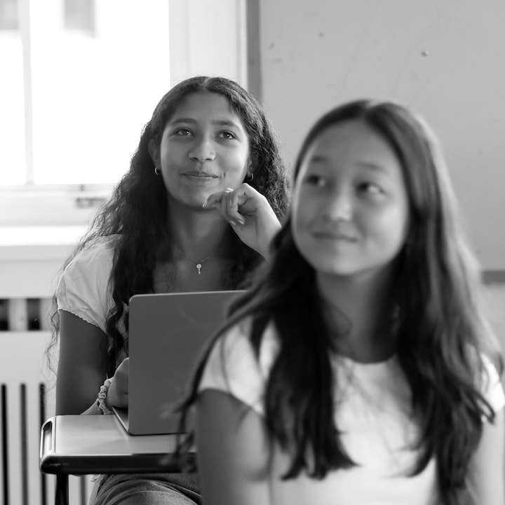 Two upper school students listening to their teacher in class with knowing smiles on their faces.