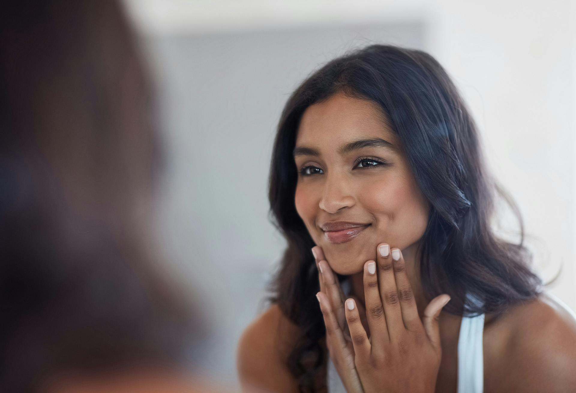 Woman looking in the mirror smiling while touching her face