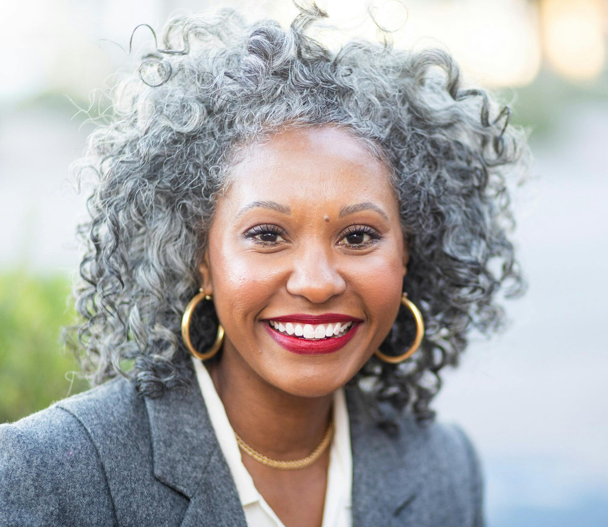 smiling woman with grey hair and hoop earrings in front of a street