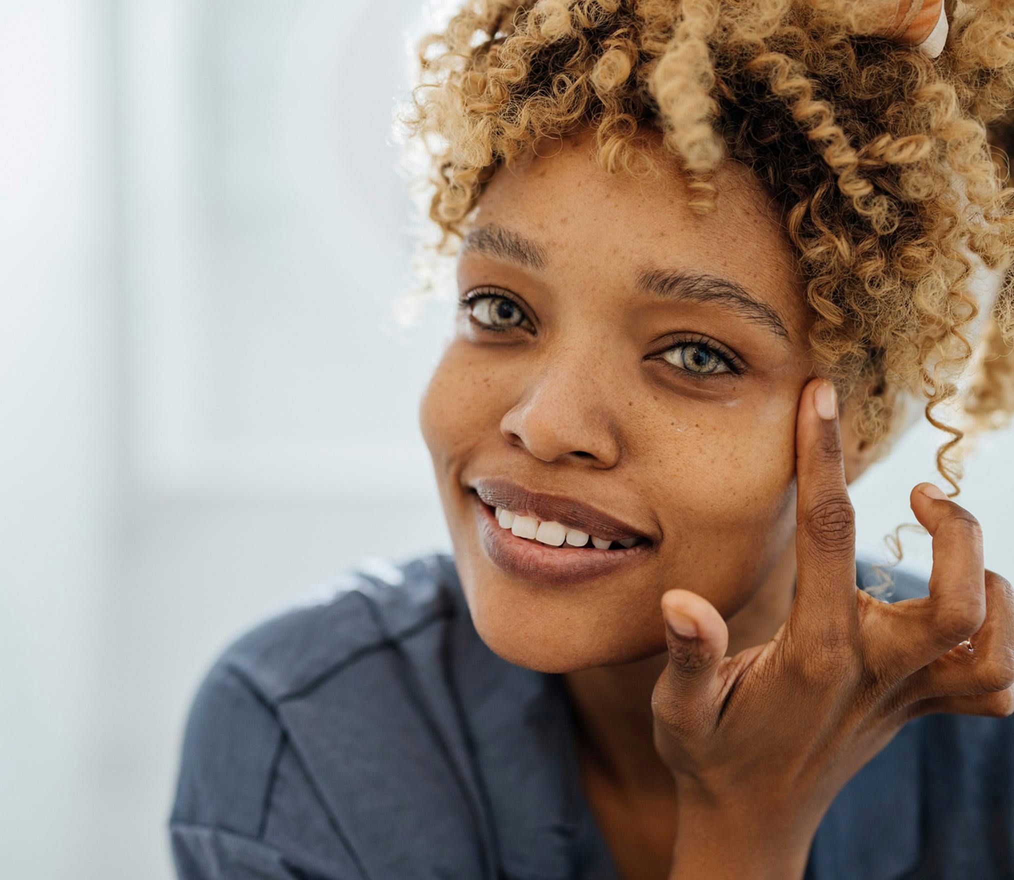 smiling woman with curly hair and blue shirt holding her hand to her face