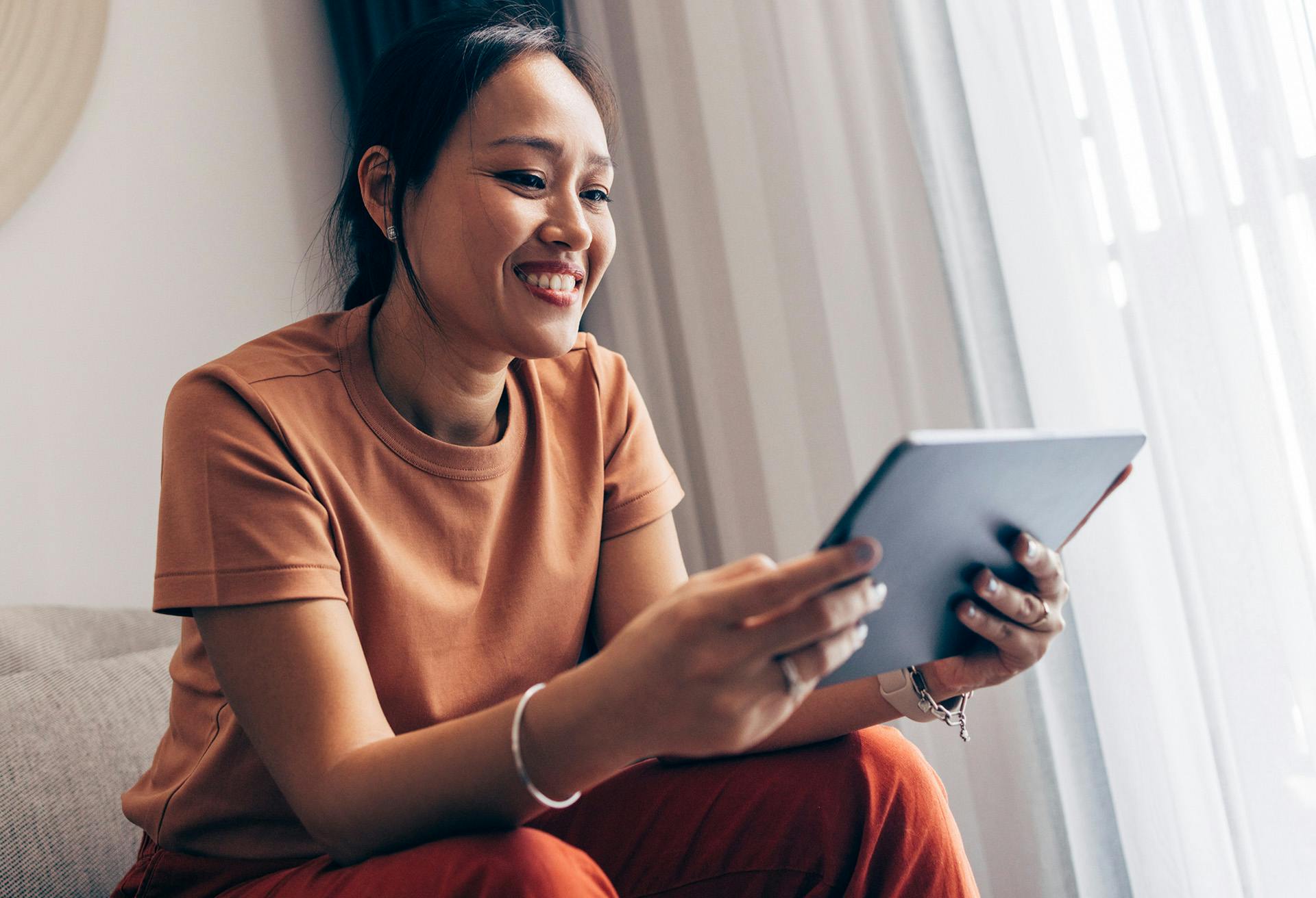 smiling woman sitting on couch using tablet computer in living room