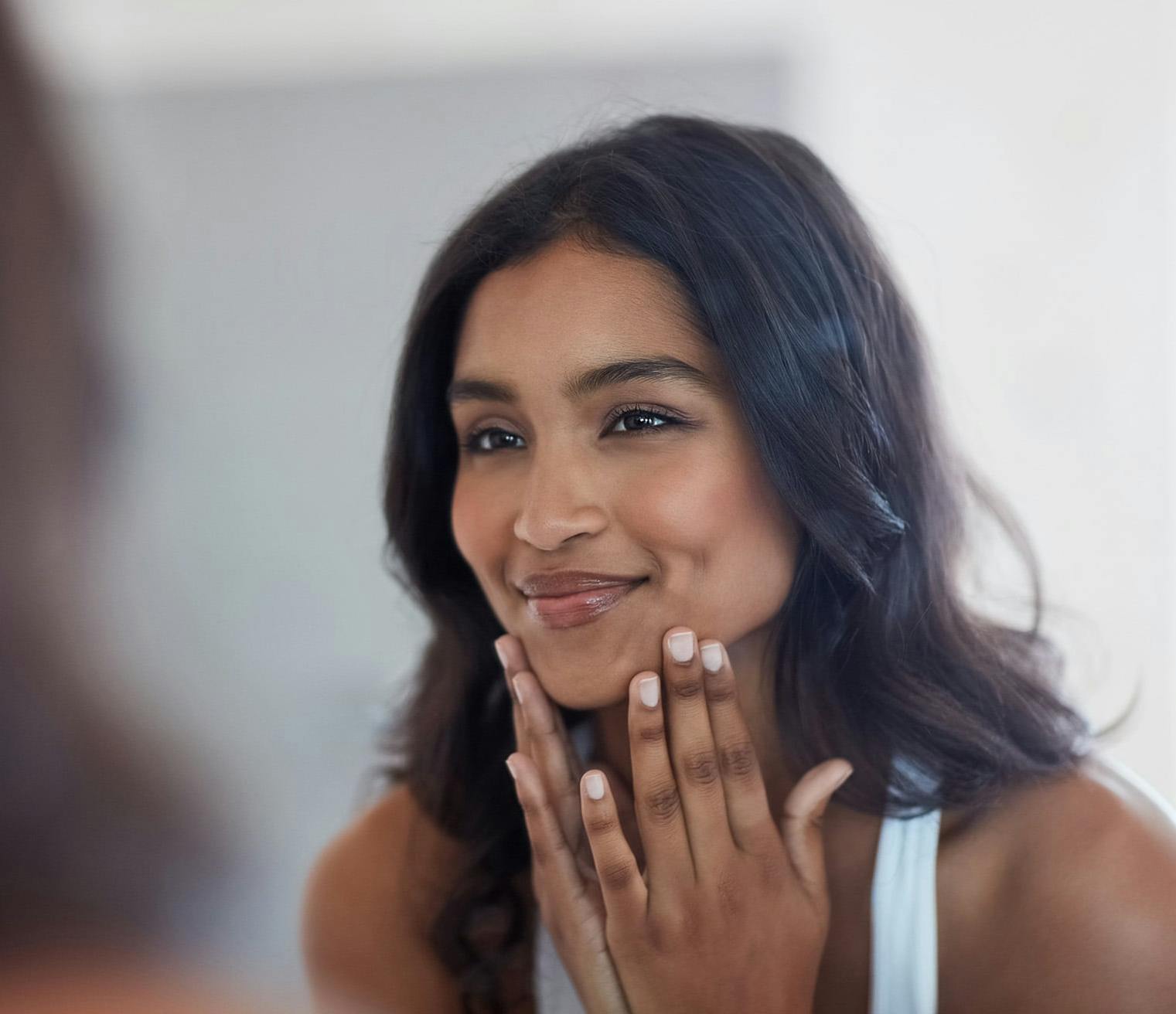 Woman looking in the mirror smiling while touching her face