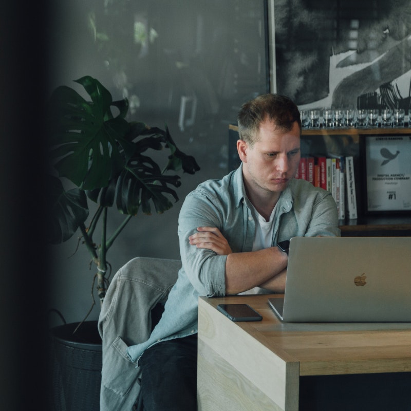 MakeReign worker sitting in office working on MacBook with background shelf displaying Loeries First Place Award Certificate