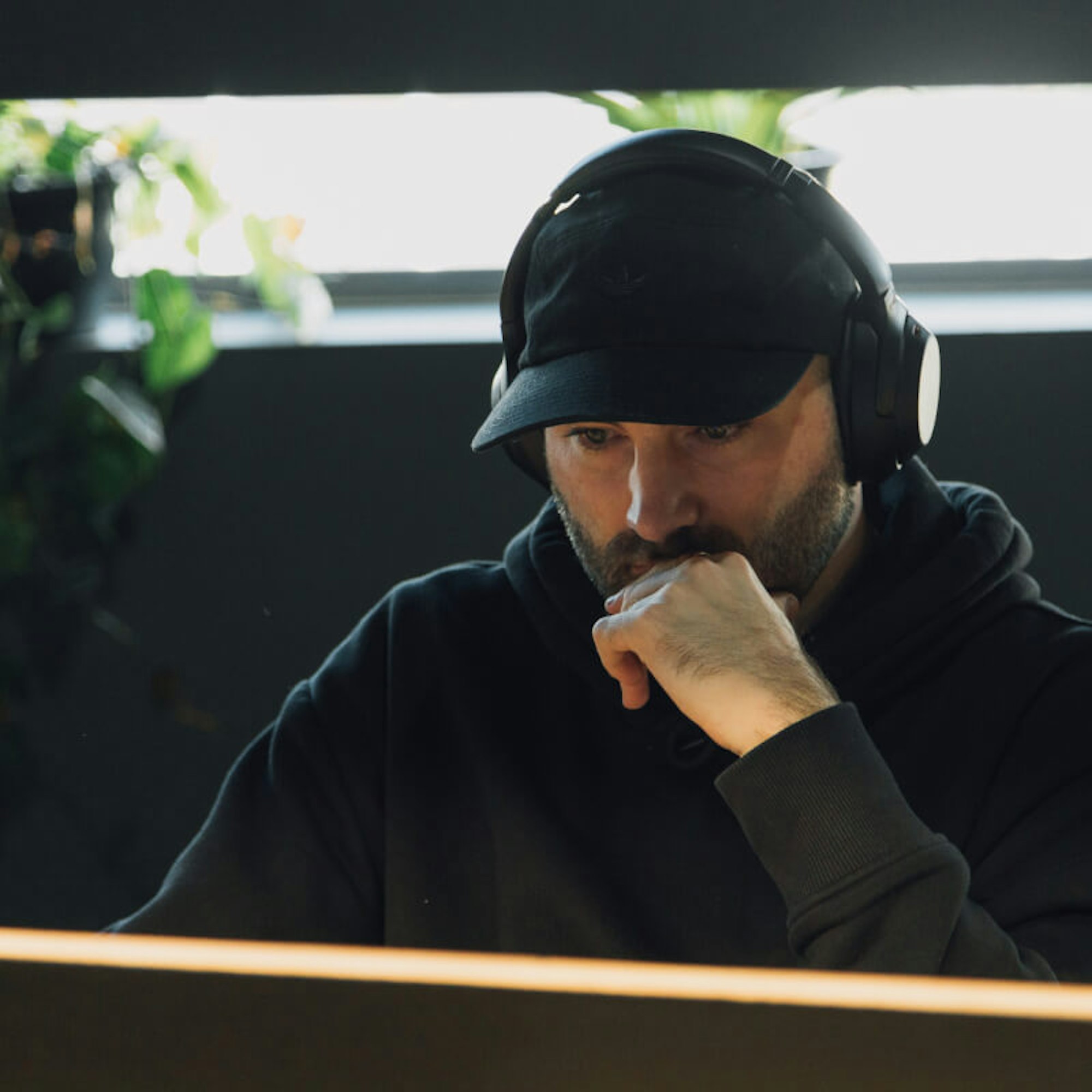 MakeReign team member with a Adidas cap and headphones working at an office with plants and a window in the background