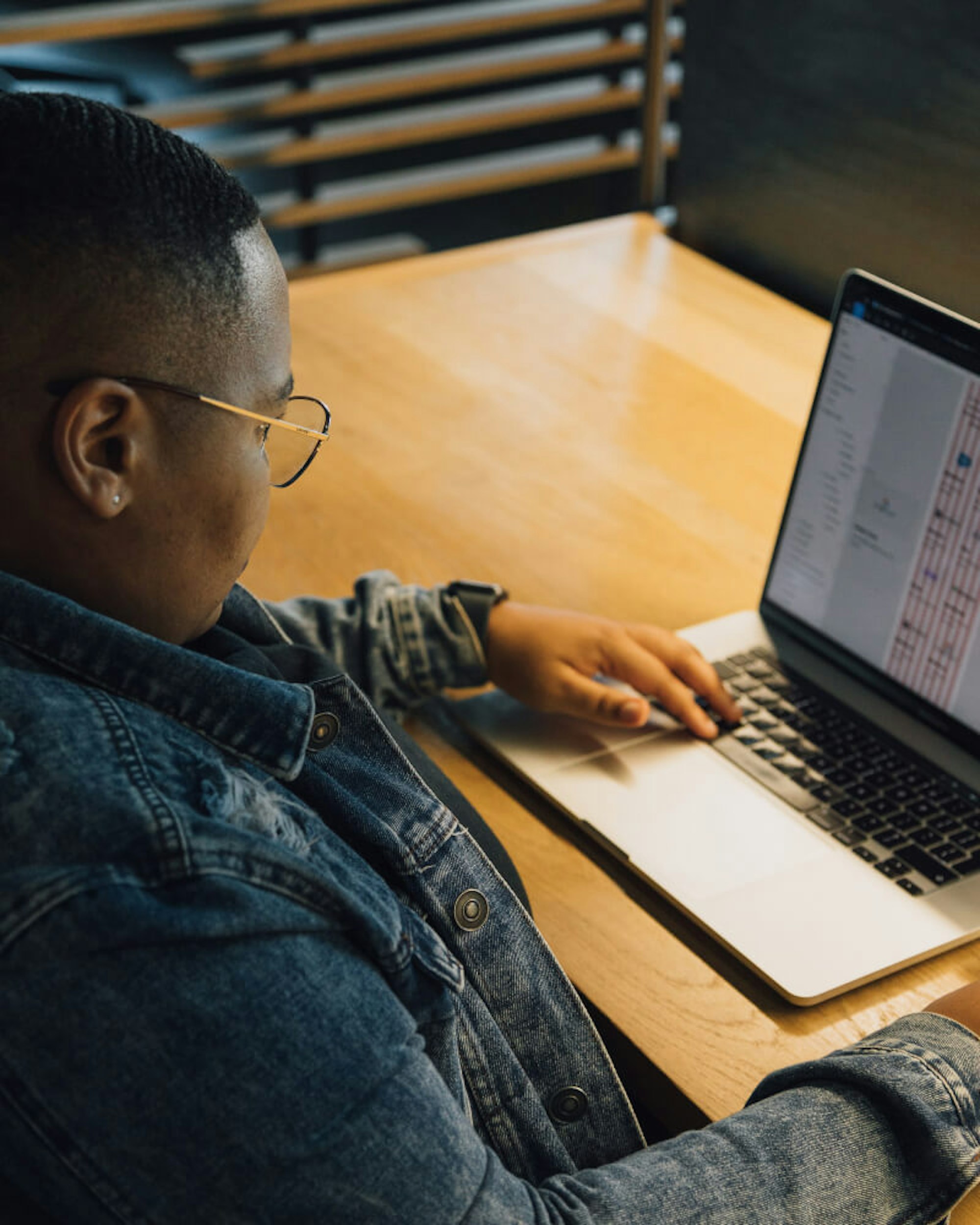 Woman with an undercut wearing glasses working at an office with a laptop on a wooden table