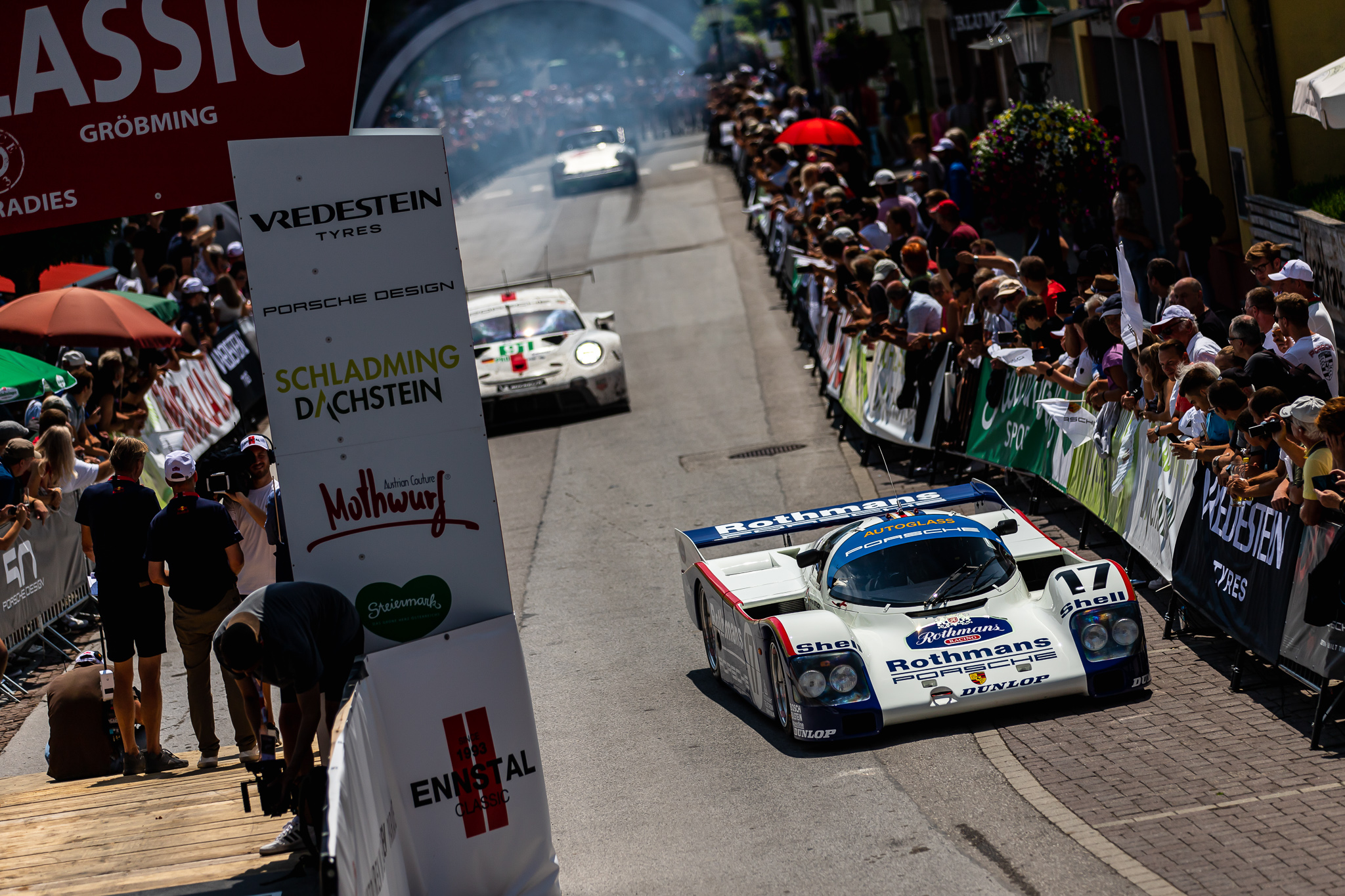 Classic race cars driving through a crowd-lined street at Ennstal-Classic rally — BUBEN&ZORWEG