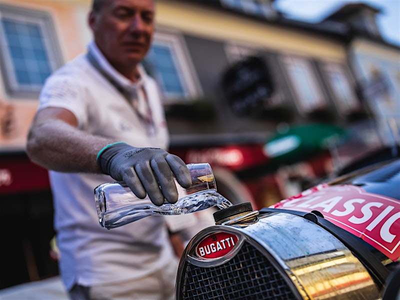 Man pouring water into a classic Bugatti car during Ennstal-Classic rally — BUBEN&ZORWEG