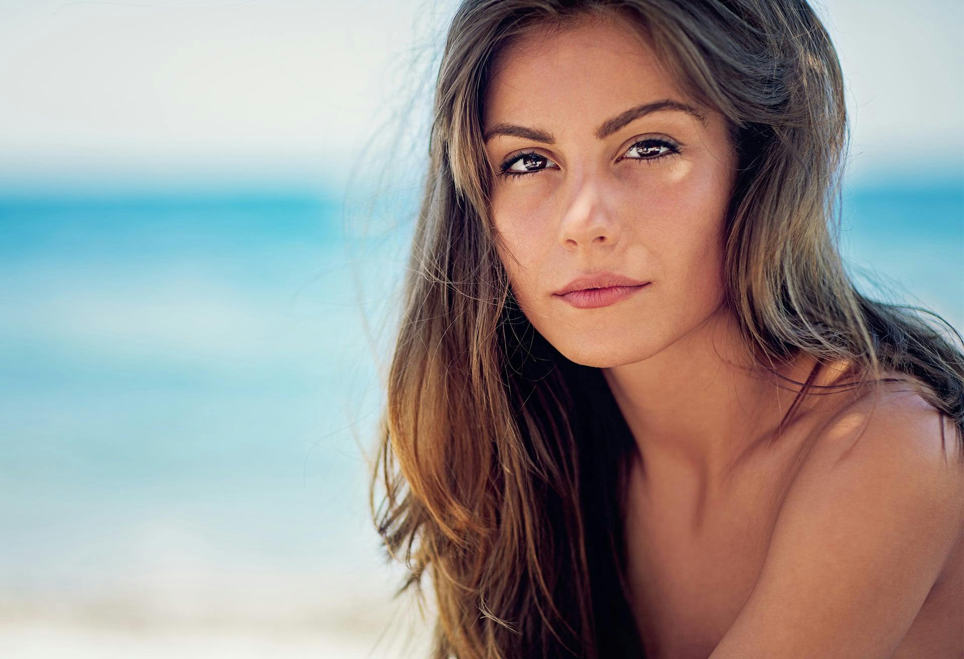 woman with brown hair and ocean in the background
