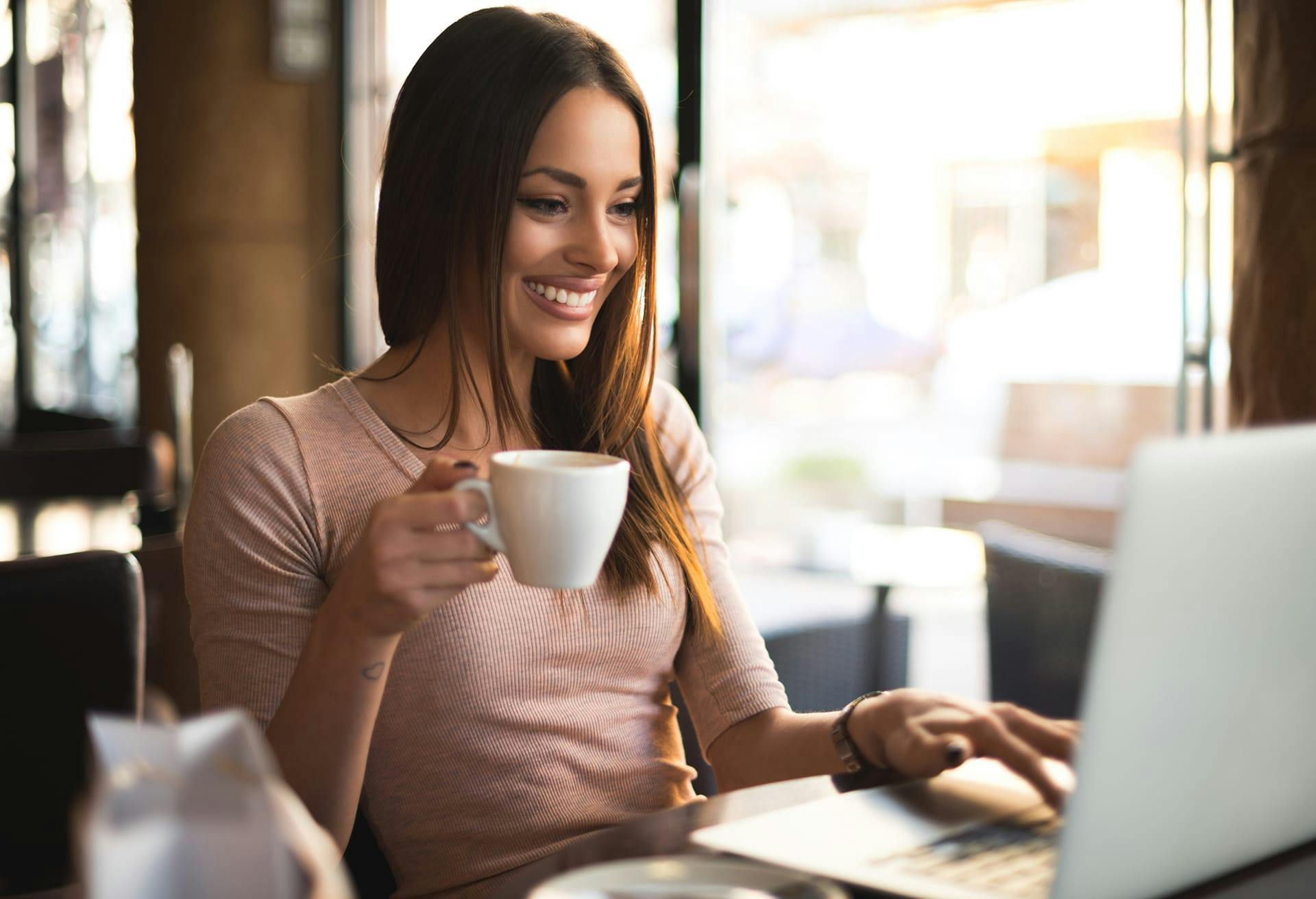 Woman with a coffee in her hand sitting in front of her laptop