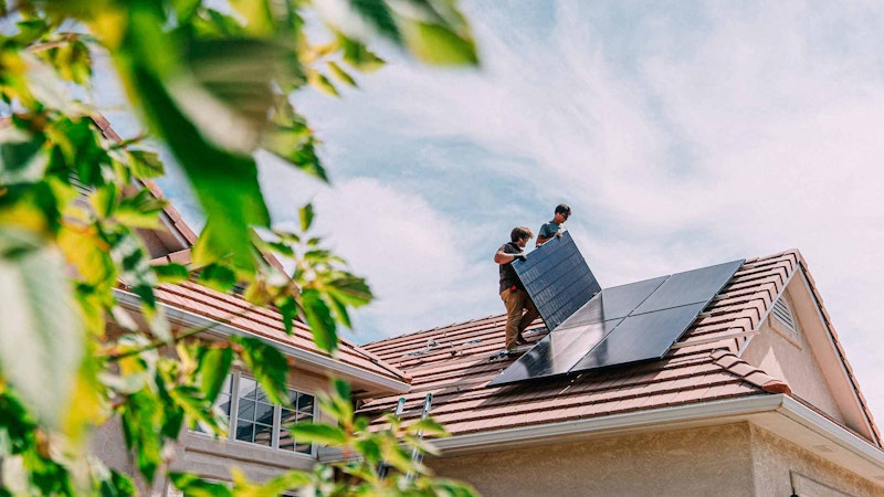 Two solar workers doing residential solar installation on a roof with a blue sky behind it.
