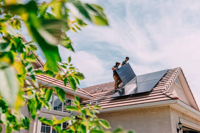Two solar workers doing residential solar installation on a roof with a blue sky behind it.