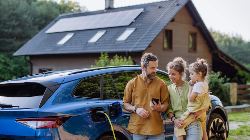 Family standing in front of their home and ev while they go over ther energy storage solutions on their phone.