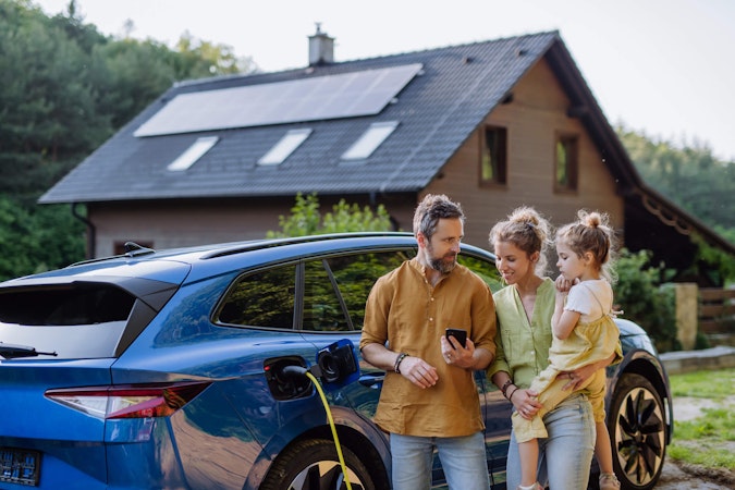Family standing in front of their home and ev while they go over ther energy storage solutions on their phone.