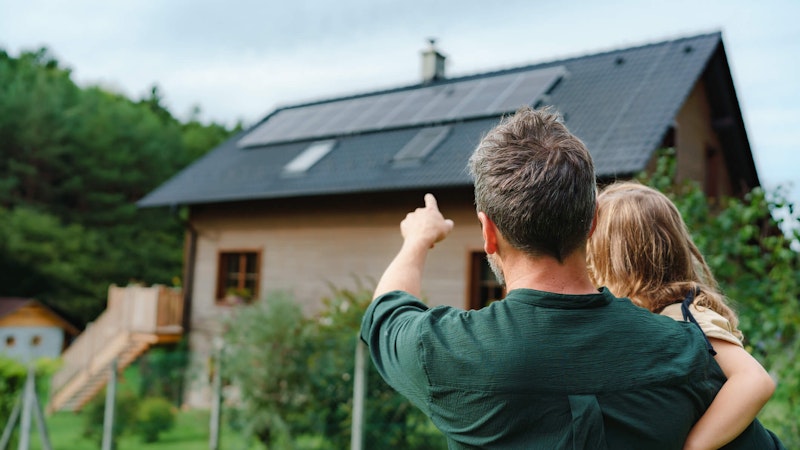 Homeowner holding a little girl while pointing to the solar installation on his roof.