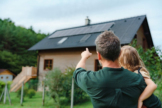 Homeowner holding a little girl while pointing to the solar installation on his roof.
