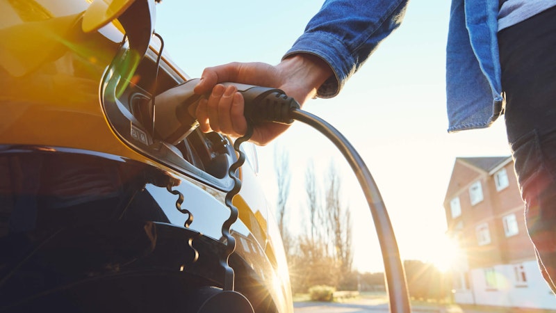 Home ev charging being plugged into a black ev while back lit by the sunrise.