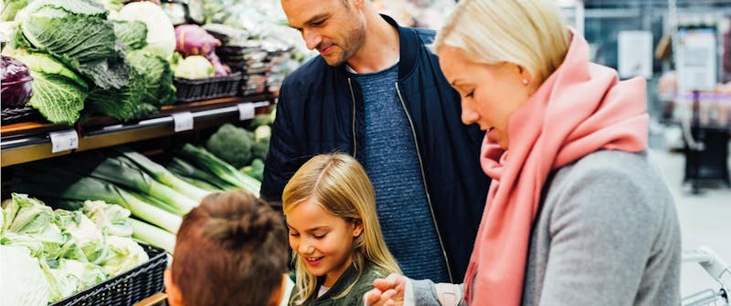 Isä, äiti ja kaksi lasta ruokakaupan vihannesosastolla.