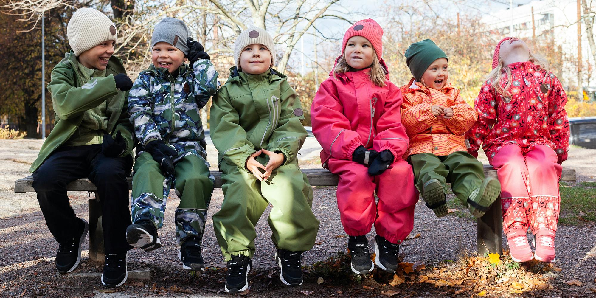 Kuusi leikki-ikäistä lasta istuvat rivissä ulkovaatteet päällä.