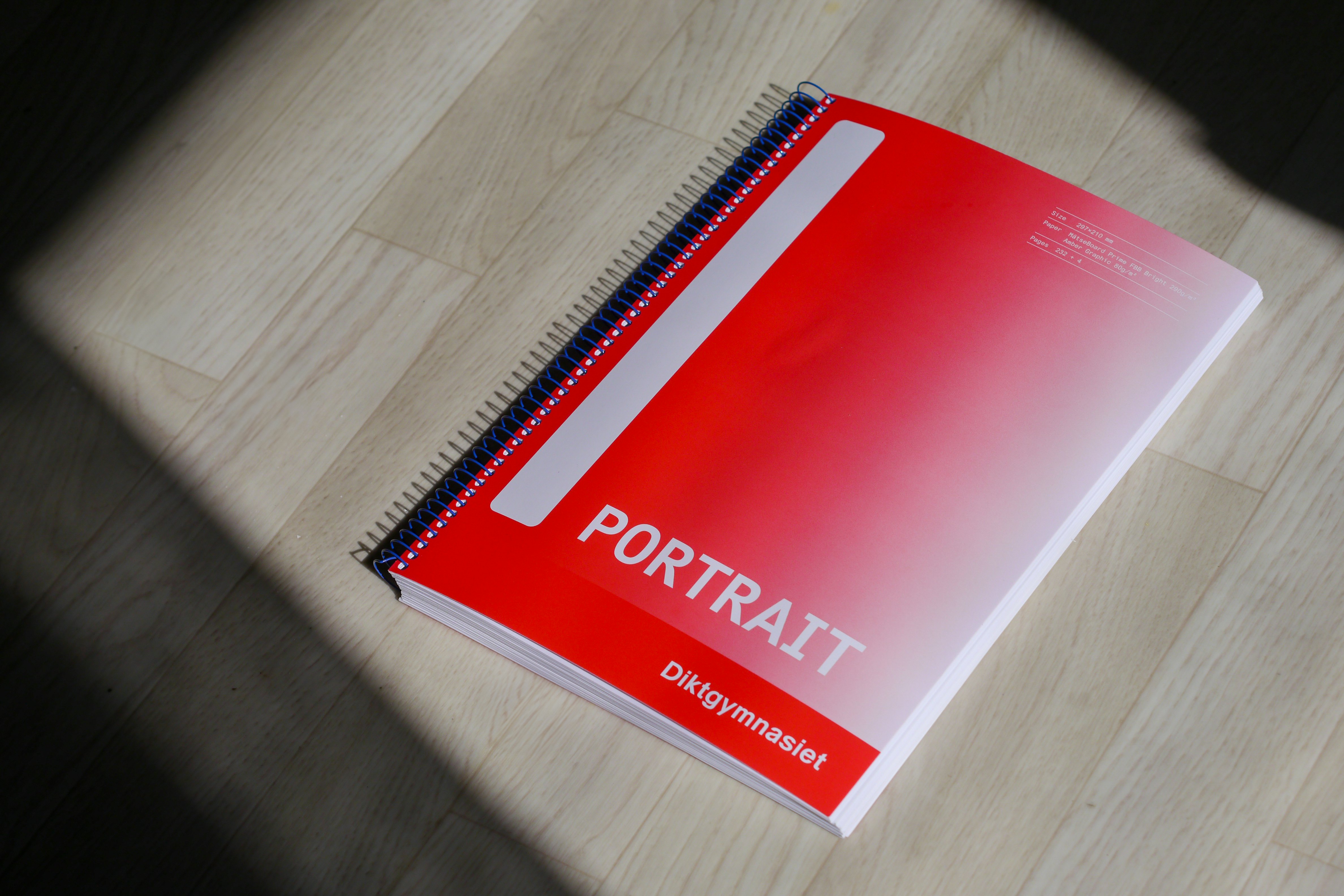Bilden visar boken Portrait som liknar ett vanligt skrivblock, liggandes i solen på ljust trägolv. Bara omslaget syns. Omslaget är rött med vit text och vita detaljer, och har en blå spiralrygg. Texten på omslaget lyder "PORTRAIT" och "Diktgymnasiet".