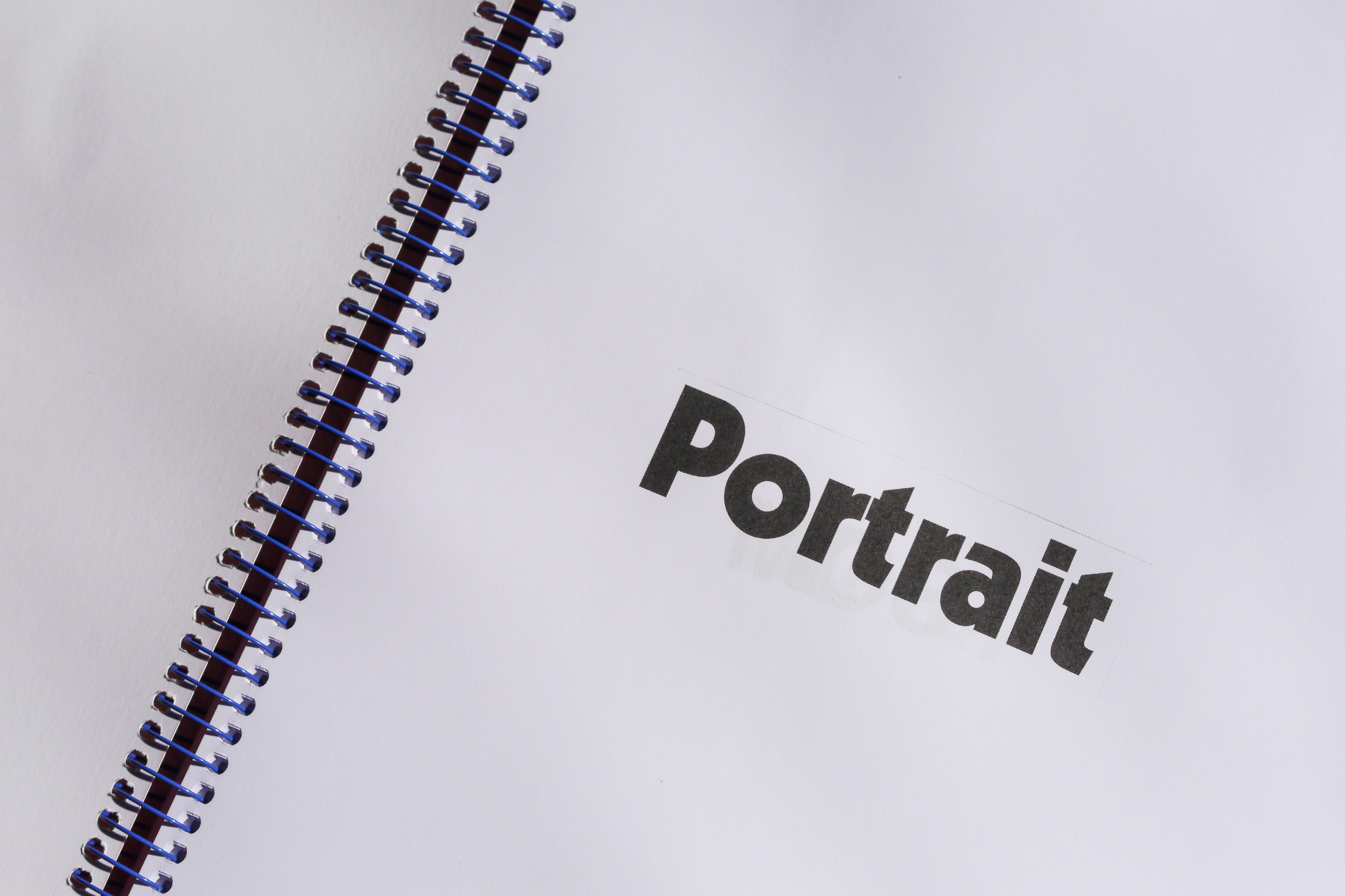 Ett bokuppslag med vita sidor och texten "Portrait" skriven i fet svart text. Sidorna sitter ihop med en blå spiralrygg.