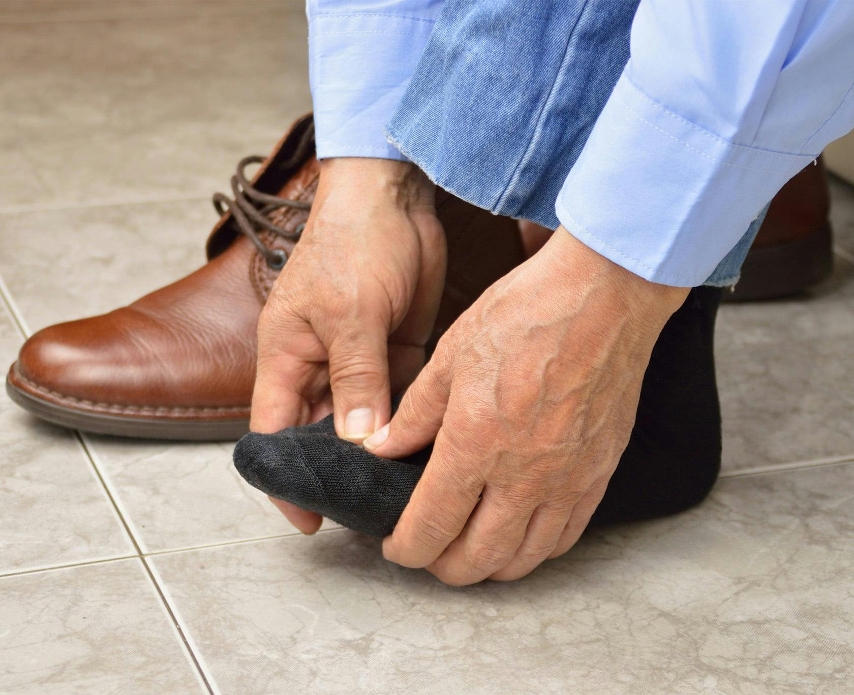 Man with his shoe off, grabbing his foot with both hands