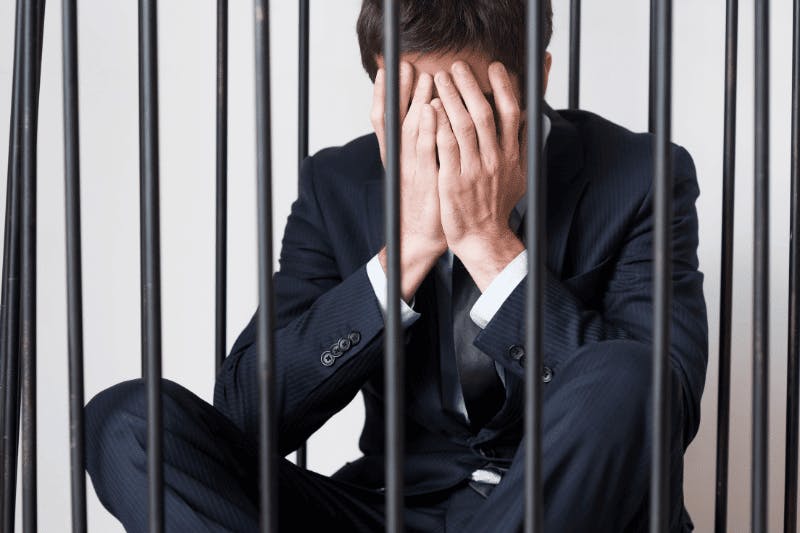 Homme enfermé dans une cage les mains couvrant son visage représentant le délit d'entrave cse