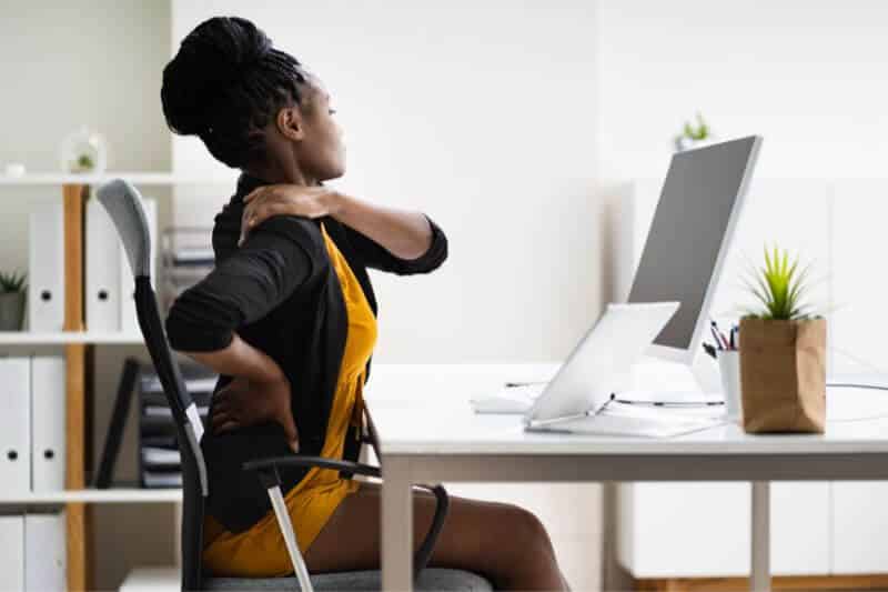 Femme assise sur une chaise qui se tient le cou suite à une douleur liée à un TMS