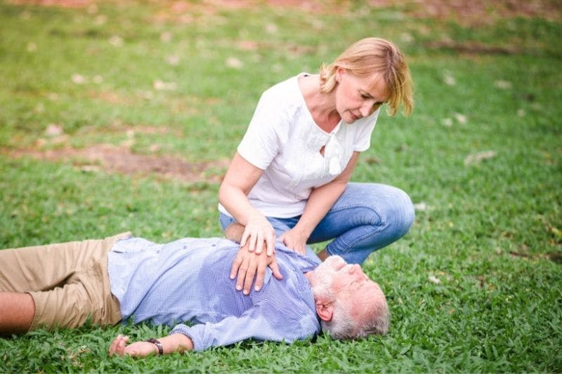 Couple de seniors futurs retraités dans l'herbe, l'homme est allongé par terre après avoir fait un arrêt cardiaque et la femme tente de le ranimer grâce aux gestes appris en formation sst