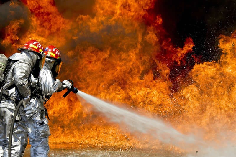 Pompiers en train d'éteindre un incendie, après l'intervention initiale des EPI et ESI qui ont suivi une formation incendie obligatoire