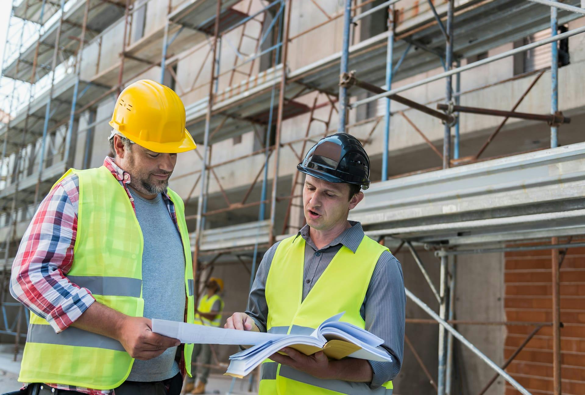 two men in safety vests and hard hats are looking at a blueprint