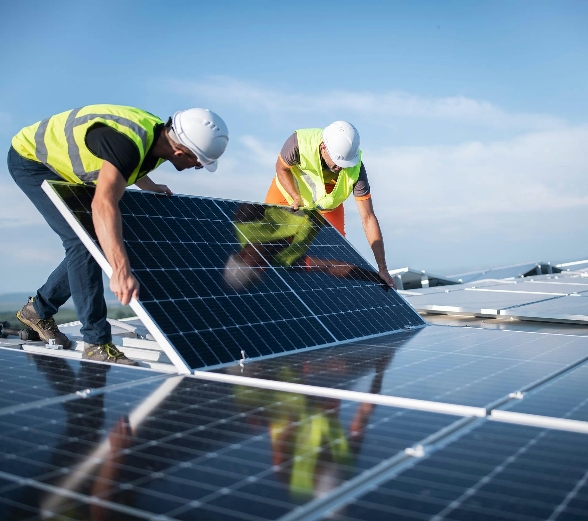 two men in safety vests are installing solar panels on a roof