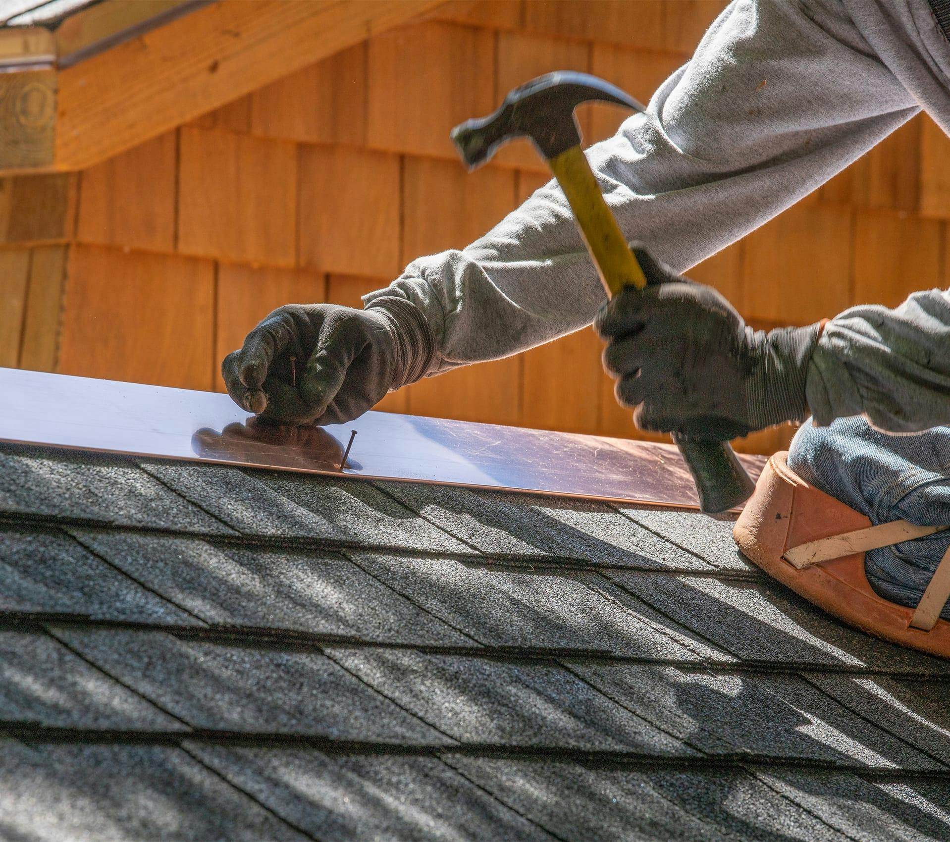 roofer using hammer to repair shinning on a house