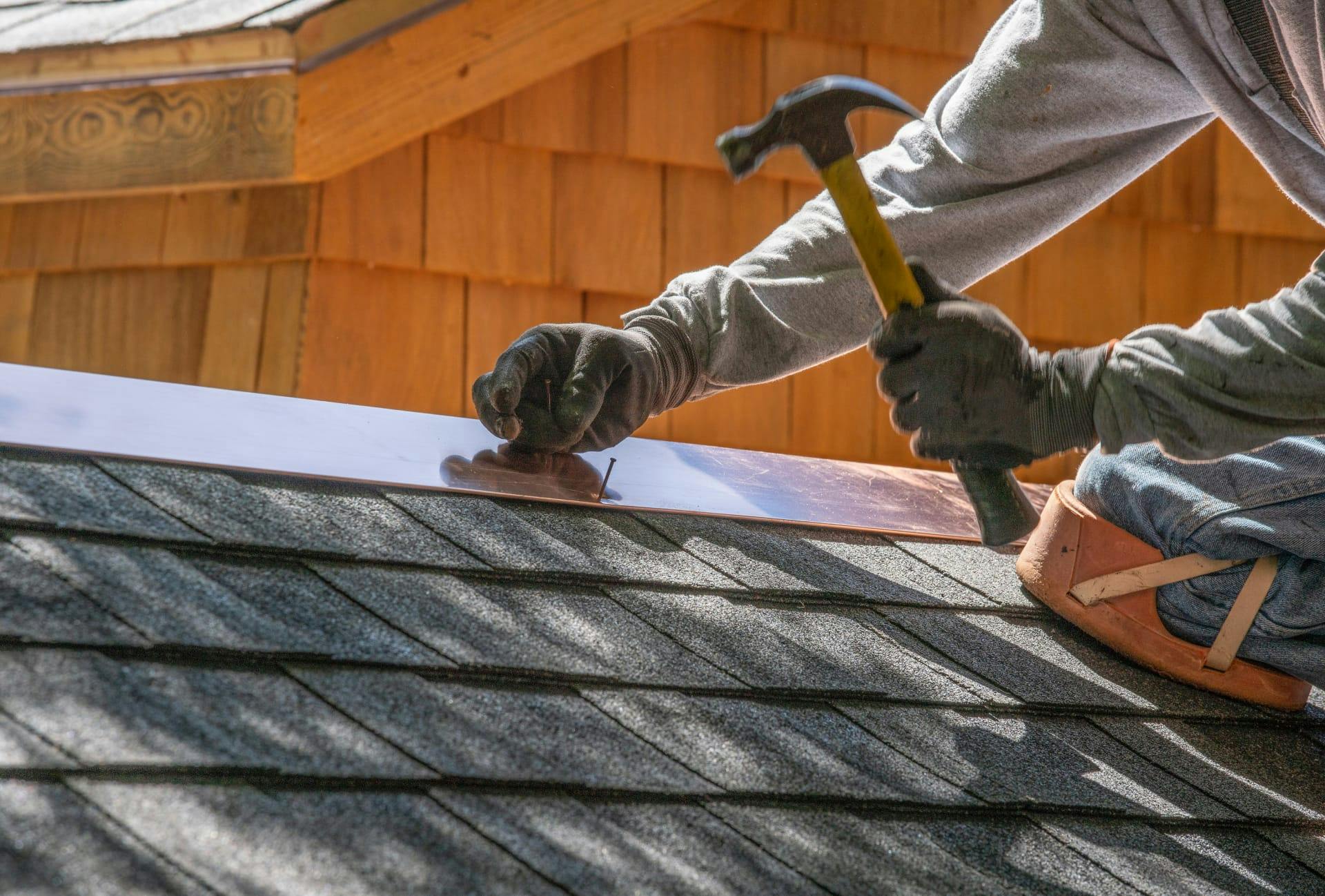 man using a hammer to nail down a shingled roof