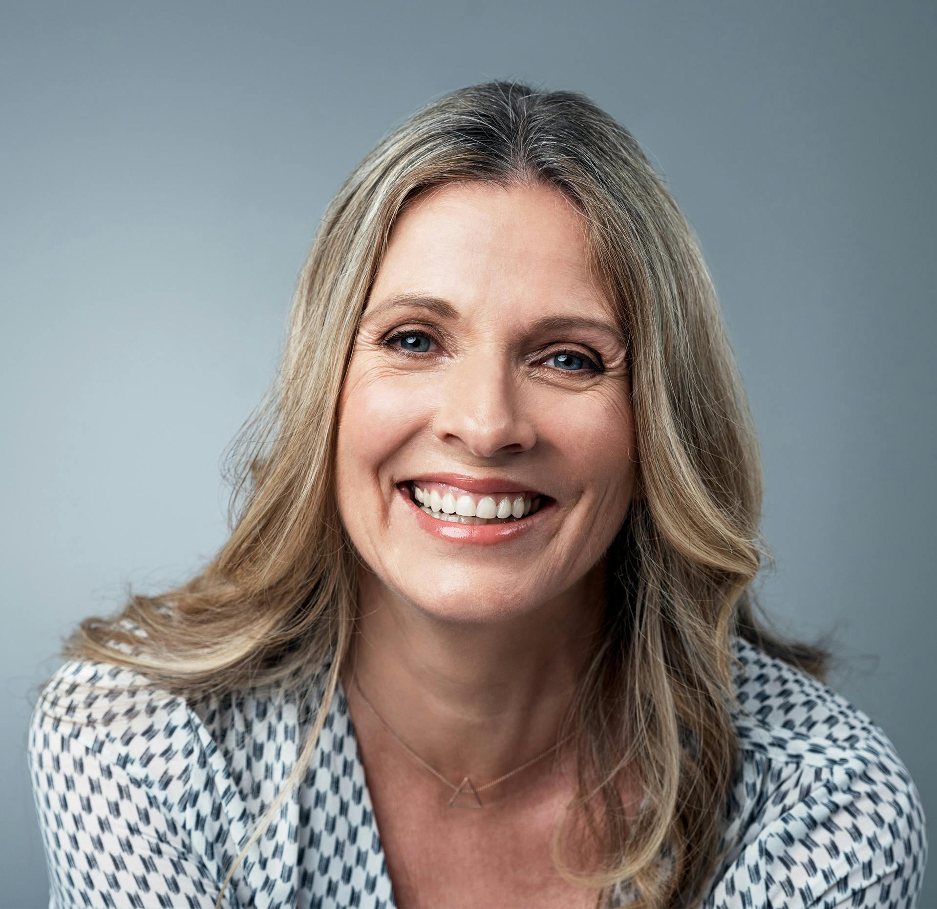 close up of a woman with long blonde hair and blue eyes wearing a white and black shirt