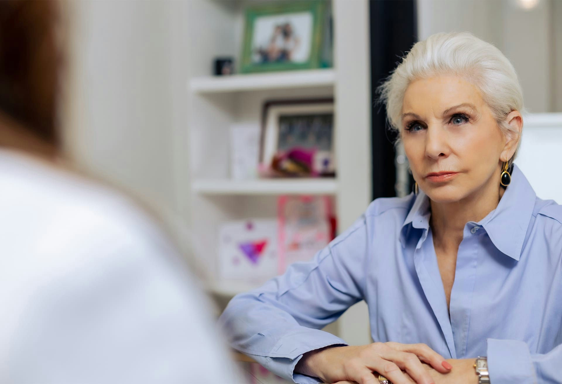 Older woman with blue button down sitting down with arms on desk