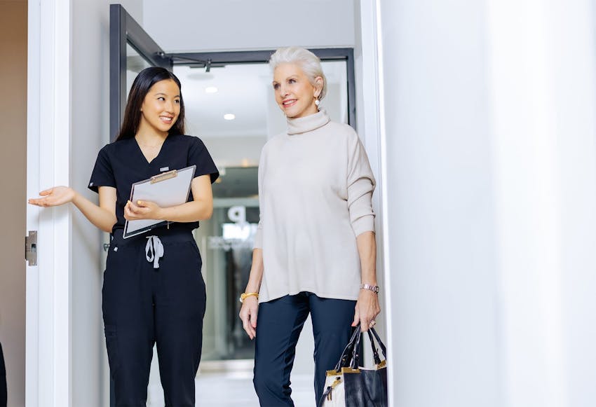 Staff member leading older woman to patient exam room