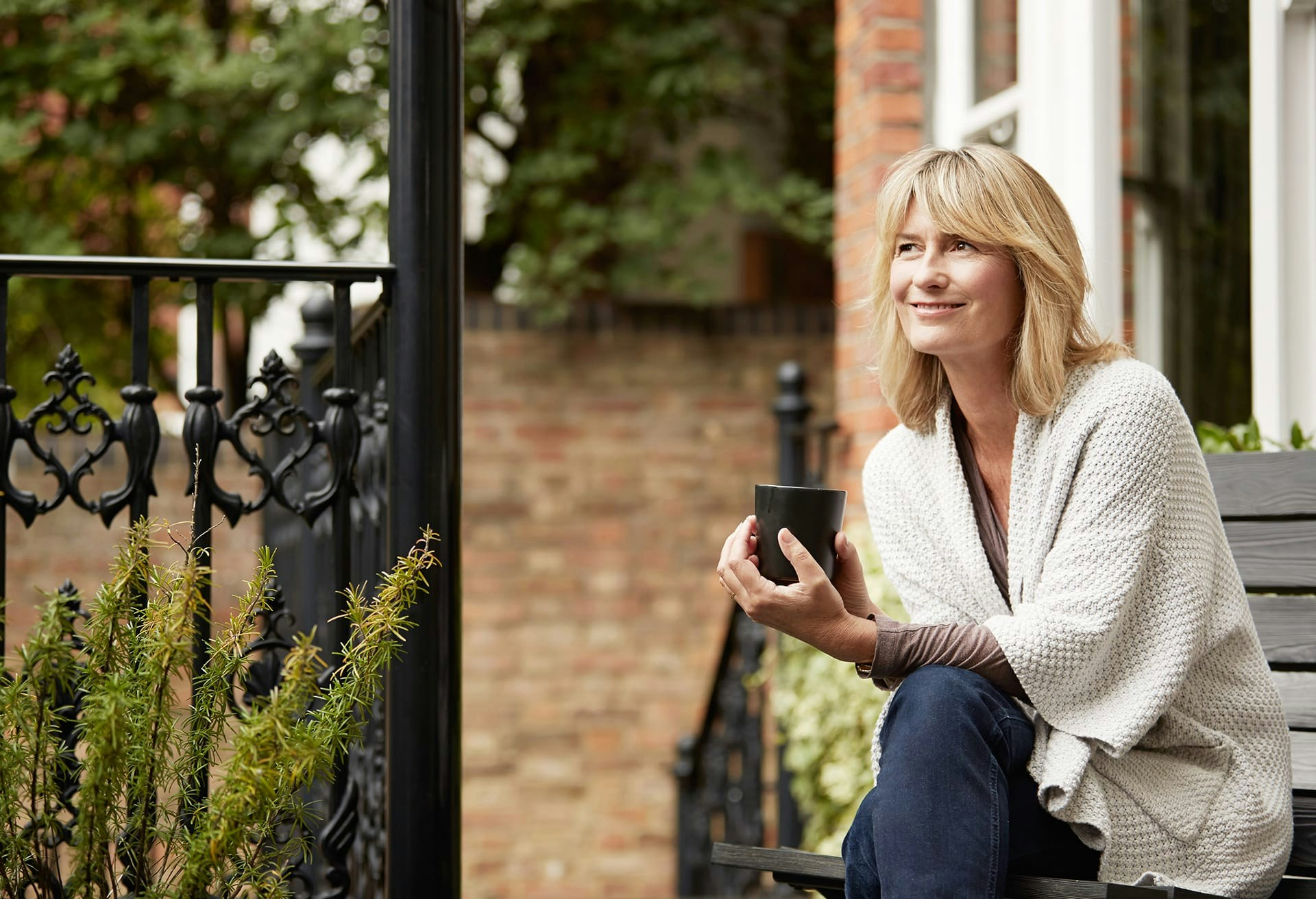 Woman sitting outside on a bench holding a cup of coffee