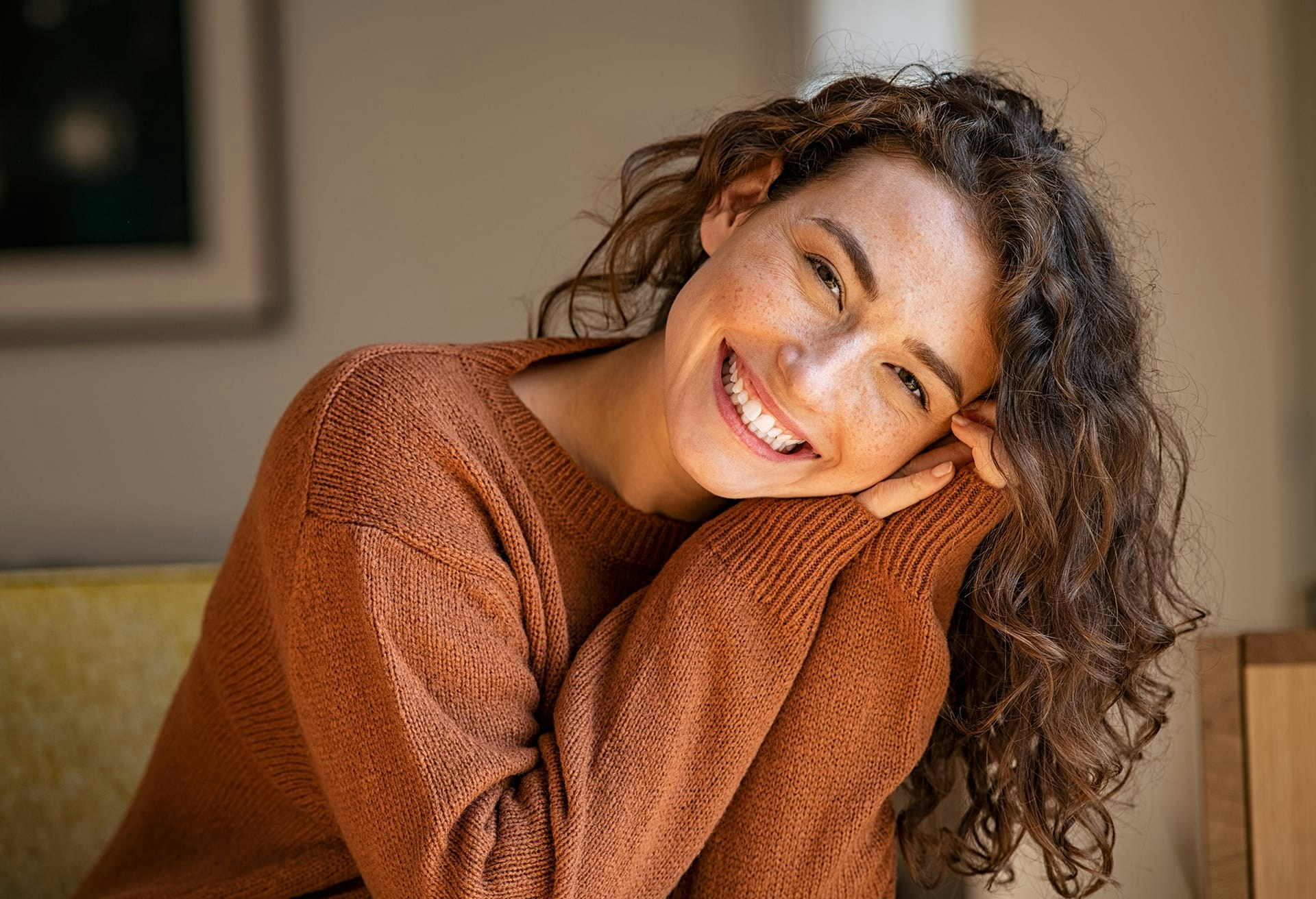 Brunette woman smiling while resting her face on her hands