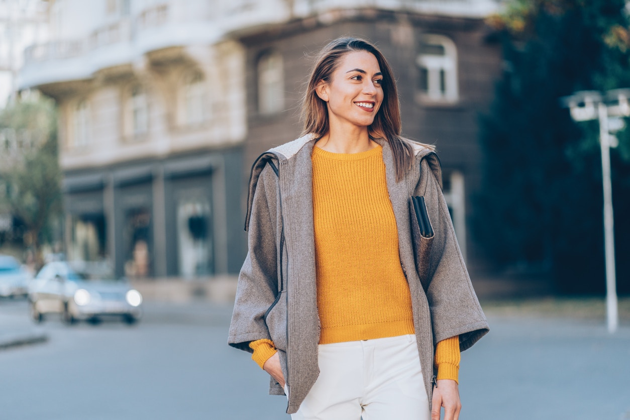 A woman in yellow sweater and beige coat walking