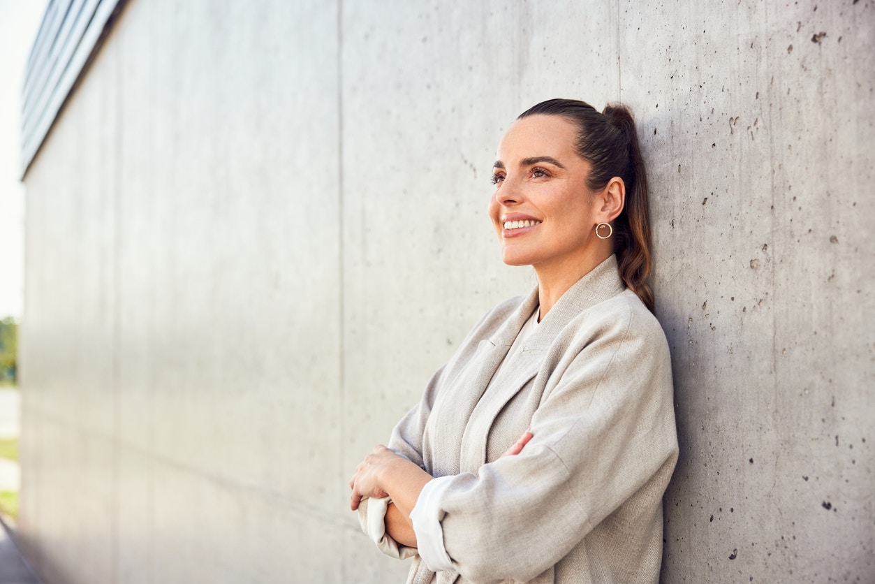 Woman in a blaser up against a wall smiling