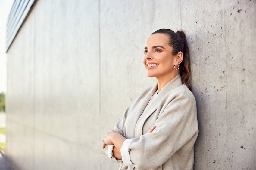 Woman in a blaser up against a wall smiling