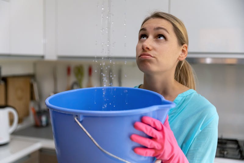 Woman holding bucket under leaking roof