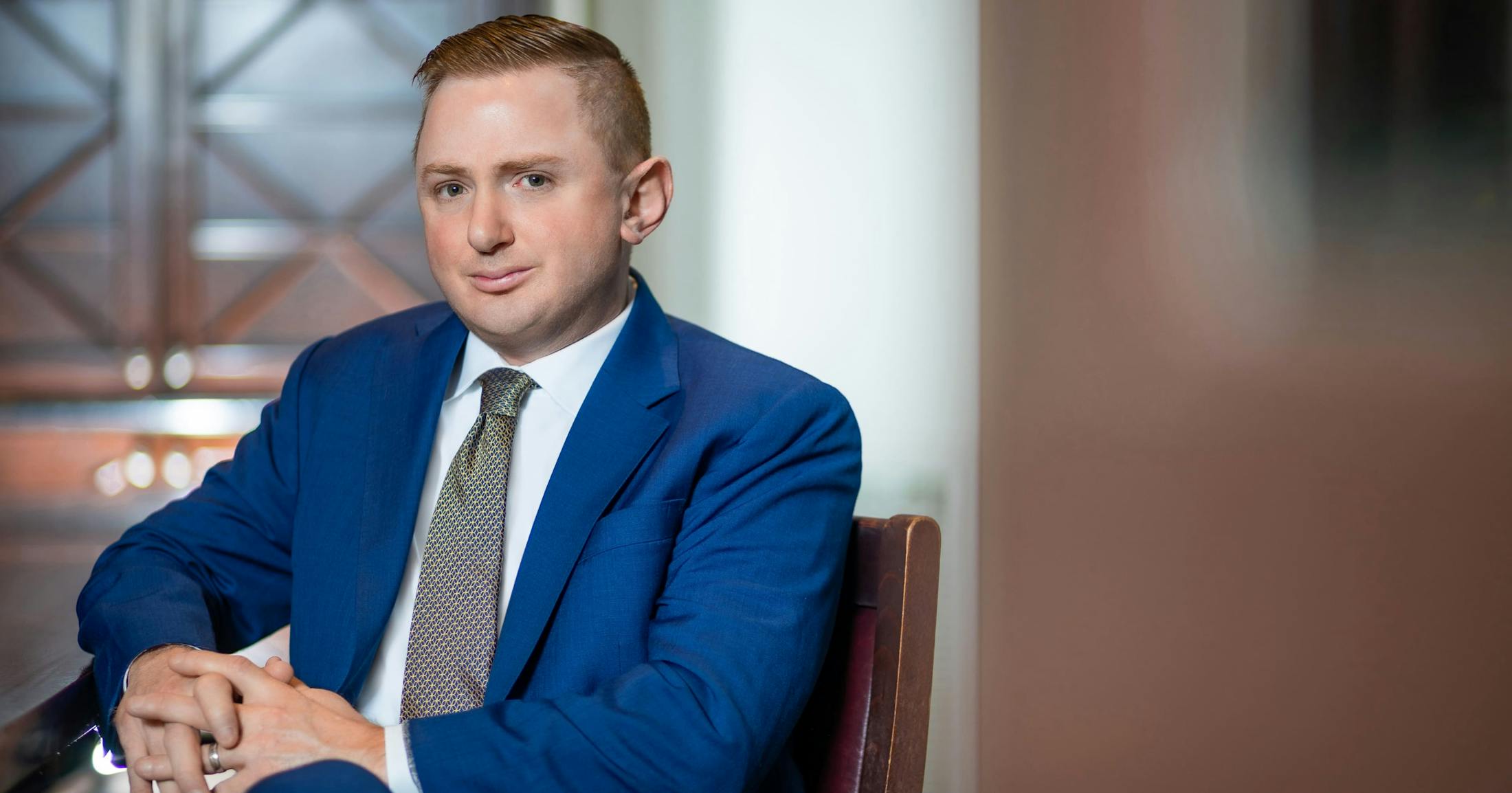 Matthew Gilman in a blue suit sitting in a chair