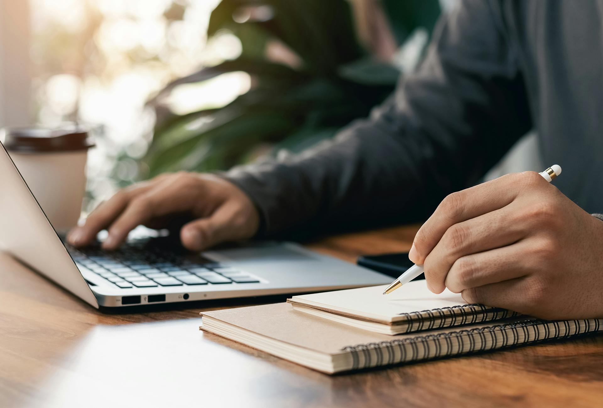 Closeup of a person working on a laptop and writing on a pad