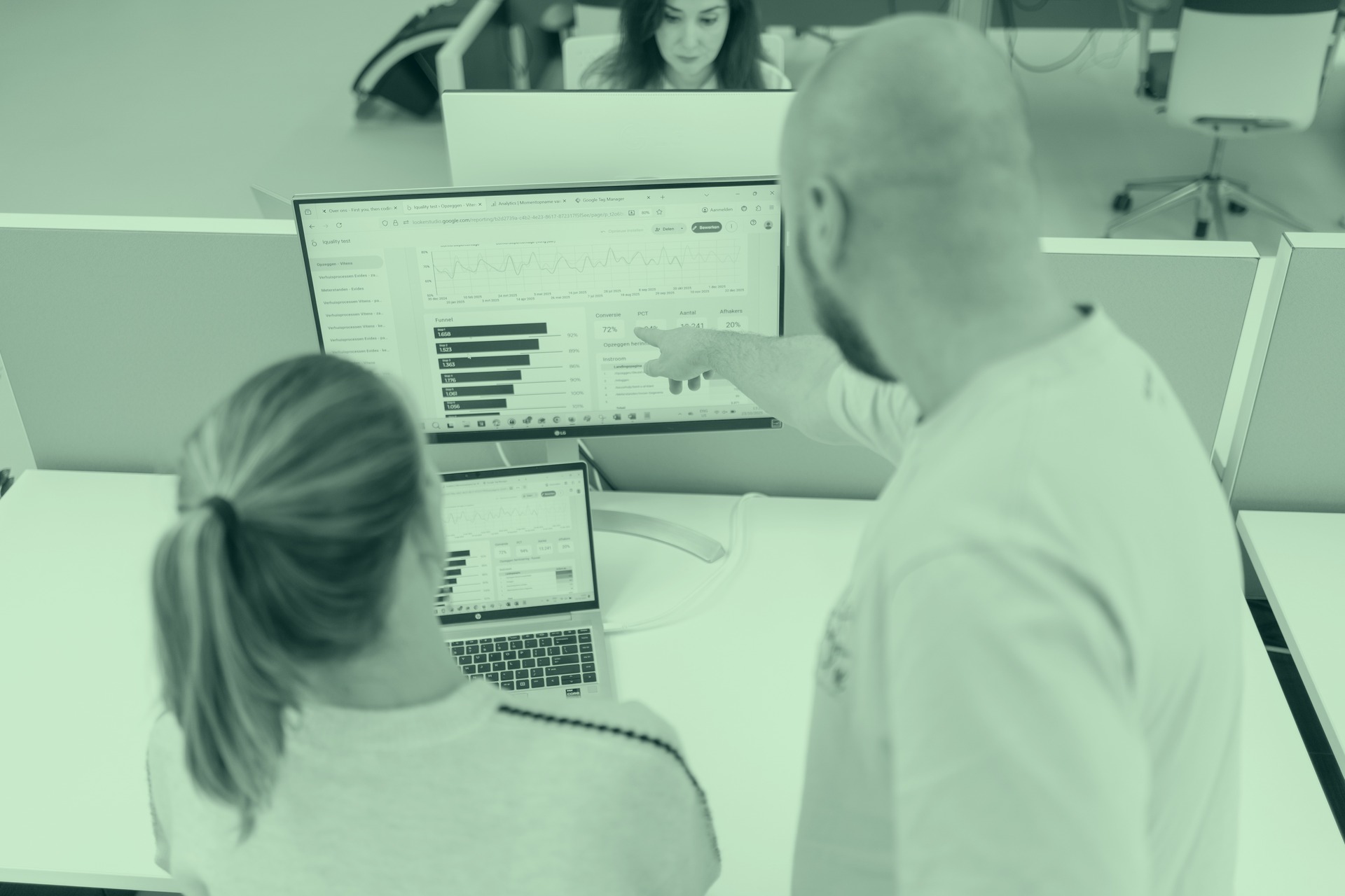 Man wijst naar Google Analytics dashboard op groot beeldscherm, collega kijkt mee