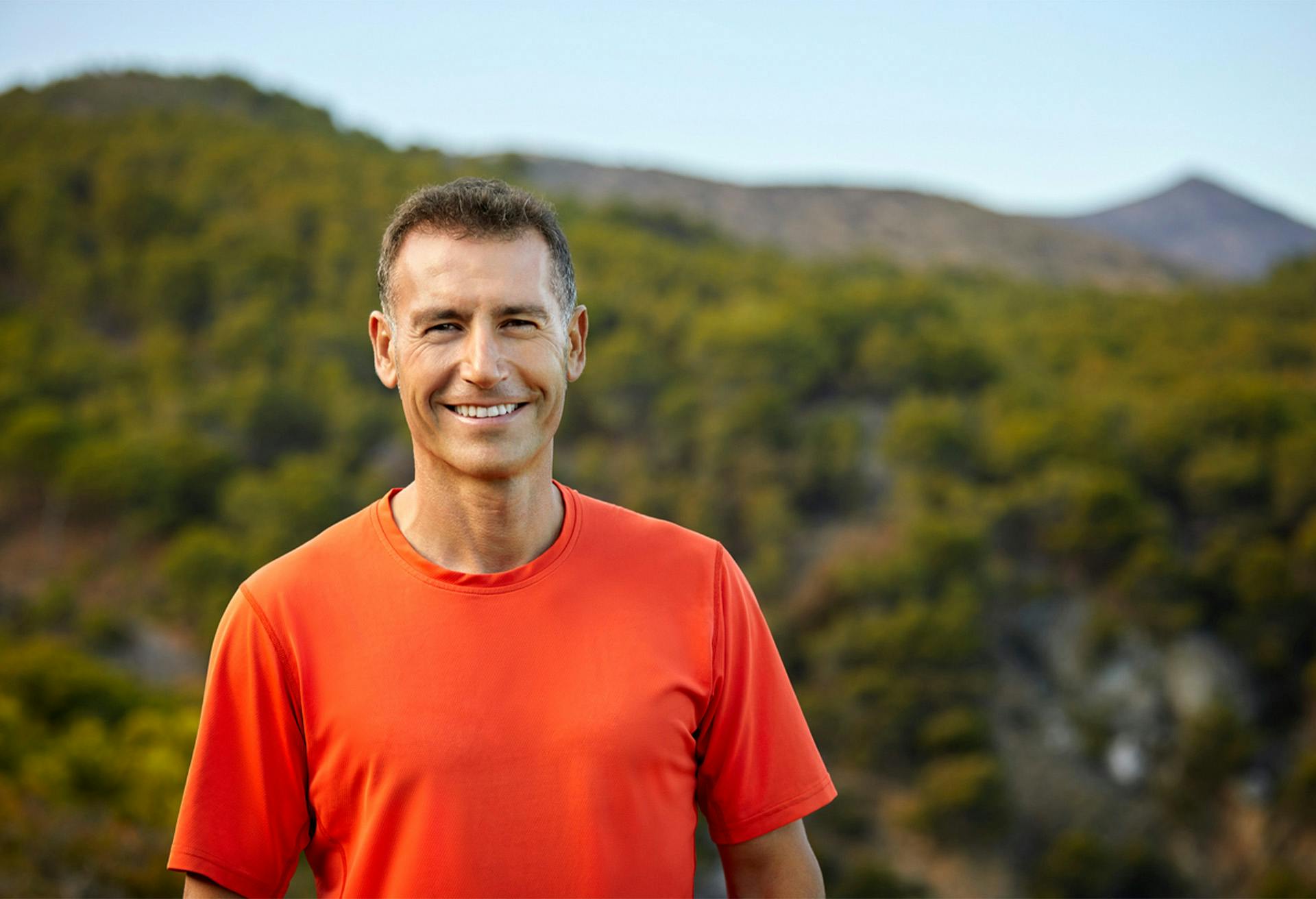 A man in orange shirt outside smiling