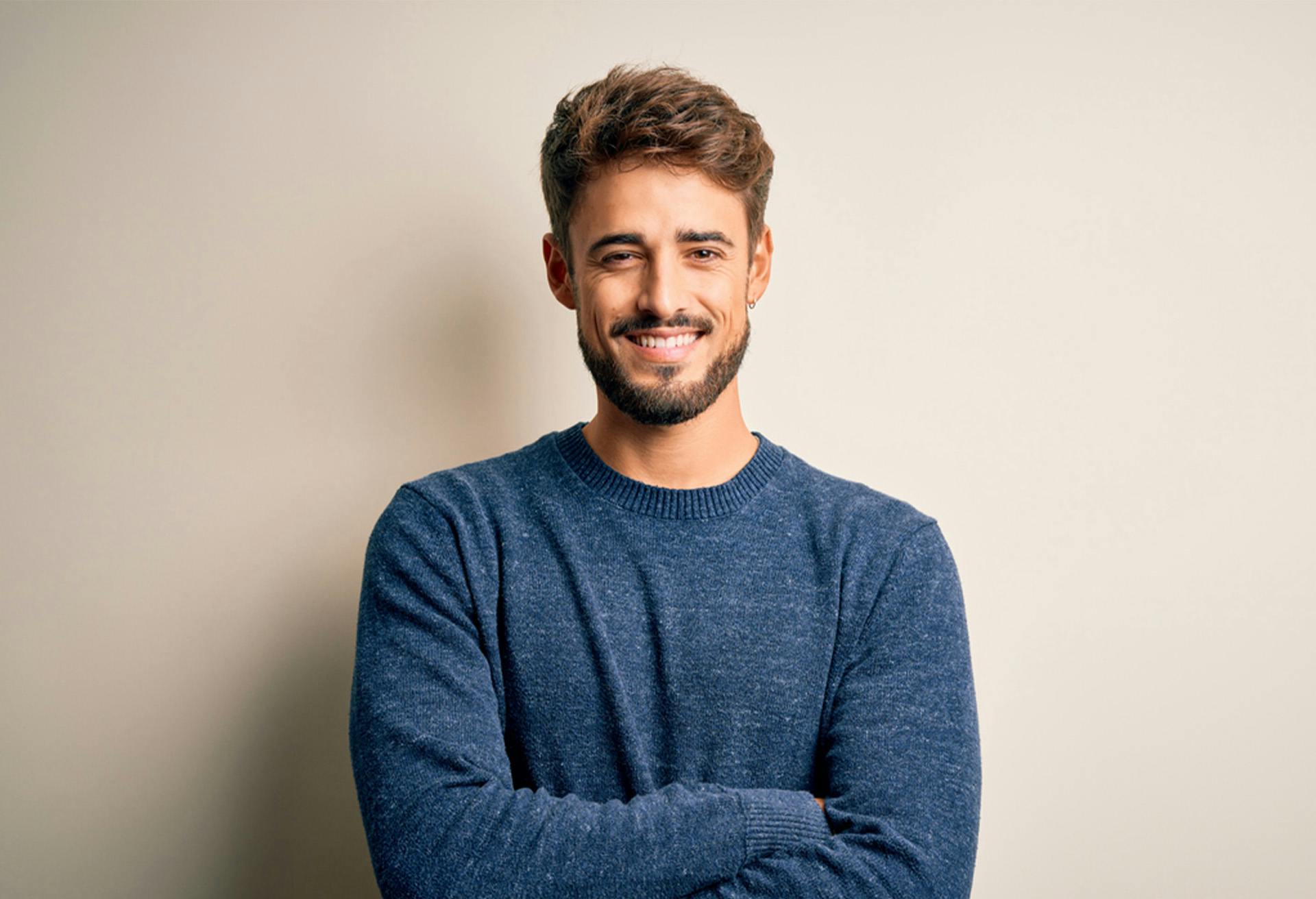 smiling man with beard and blue sweater standing with arms crossed